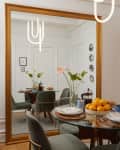 The large mirror reflected a dining room table with four green chairs around a glass dining room table.