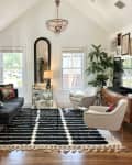 Living room with large black and white area rug with black couch and white lounge chairs. Across from a gallery wall.
