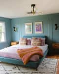 Green painted bedroom with colorfully made bed.