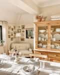beige dining room with large wood table with pale tablecloth, large wood hutch, cozy corner chair, and gray chandelier
