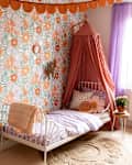 Bed place in corner of child's bedroom with floral wallpaper.