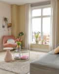 Circular glass coffee table holds vase with tulips in living room with gray modular sofa and pink accent chair.