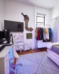White bedroom with clothing rack, television on distressed dresser, and desk.