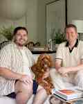 Two men with brown dog sitting on white couch