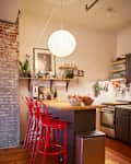 Red stools surround a dining table with stainless steel coffee maker.
