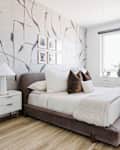 White bedroom with one gray and white patterned wallpaper wall, gray velvet bed, and other velvet accents