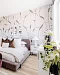 White bedroom with one gray and white patterned wallpaper wall, gray velvet bed, and other velvet accents