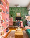 A living room with a green fabric couch across from a pink bookcase and gallery wall