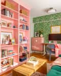 A living room with a green fabric couch across from a pink bookcase and gallery wall