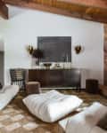 Red wood ceiling with large beams, brick accent wall with tv, brown and cream checkered rug, soft white modern shaped couches