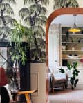 Arched doorway between room with wallpaper and wainscoting and room with built-in shelving.