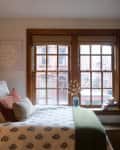 White bedroom with wainscoted walls, vintage furniture, and wood window trim