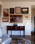 Living room with a gallery wall of framed art, a wooden console table, gray armchair, and brown leather sofa.