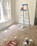 Ladder in living room with paint buckets on the floor before renovation.