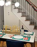 Dining area with a white table set for a festive meal, featuring blue chairs, green and red decor, and a candle centerpiece.