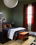 Cozy bedroom with a green wall, a bed with patterned bedding, a wooden trunk, and a folding screen.