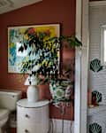 Bathroom with terracotta walls, a potted plant, a white toilet, and a shower featuring hexagonal tiles and green shell designs.
