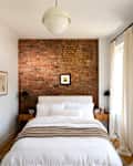 Cozy bedroom featuring a brick accent wall, white bedding, wooden nightstands, and sheer curtains.