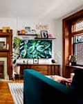 Cozy living room featuring orange velvet chairs, a round black table, a wooden mantel, and a large TV displaying green leaves.
