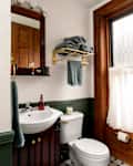 Small bathroom featuring a white sink, toilet, wooden accents, green trim, and a window with sheer curtains.