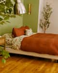 Cozy bedroom featuring a brown comforter, floral sheets, wooden nightstand, and greenery.