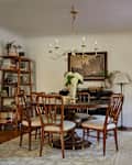 Dining room featuring a round wooden table with six chairs, a chandelier, and a bookshelf filled with books.