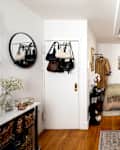 Cozy kitchen area with a round mirror, hanging bags, and a small dining space featuring a green blanket and decorative plates.