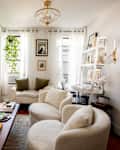 Cozy living room with a chandelier, two round chairs, a white sofa, and a wooden coffee table adorned with books and decor.