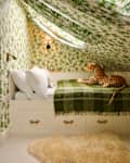 Cozy attic bedroom with green leaf-patterned wallpaper, a bed with white pillows, a green throw, and a plush leopard toy.