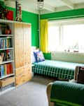 A bedroom with green walla snd large cabinets with unpainted doors separated by a bookshelf.