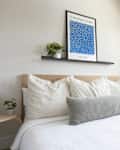 Cozy bedroom featuring a bed with striped pillows, a gray lumbar pillow, a plant, and a blue art print on the wall.