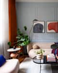 Cozy living room featuring a beige sofa, colorful throw, modern coffee table with books, and large plants.