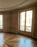 Spacious room with ornate molding, large windows, a fireplace, and herringbone wood flooring.