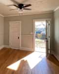 Empty room with light green walls, hardwood floor, ceiling fan, and a door leading outside.