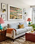 Bright living room featuring a patterned sofa, colorful artwork, and a small dining table with plants.