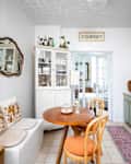 A kitchen with a round wooden table, two chairs, a white cabinet, and floral-patterned cabinets.