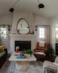 Dark sofa in front of windows in light living room with boucle chair, leather chair and ottoman, marble coffee table, and mirror above fireplace.