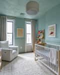 Nursery with light blue walls, a white crib, a cozy armchair, and framed children's artwork.