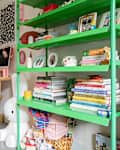 Colorful home office with a green bookshelf, yellow chair, and a computer, featuring books, decor, and clothing.