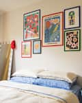 Cozy bedroom with a bed featuring blue and cream bedding, colorful wall art, a mirror, and a side table with decor.