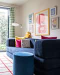 Bright living room with a blue corduroy sofa, colorful cushions, striped curtains, and a cheerful yellow smiley ball.