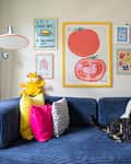 Cozy living room with a blue sofa, colorful pillows, a dog lounging, and vibrant wall art featuring food themes.