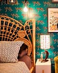 Colorful bedroom with a rattan bed, teal leopard-print wallpaper, a green sofa, and decorative art.