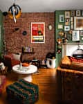 Cozy living room with green walls, brick accents, eclectic art, a white coffee table, and colorful textiles.