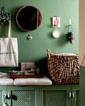 Entryway with green walls, a round mirror, a woven basket, and decorative items on a green cabinet.