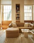 Cozy living room featuring a curved beige sofa, wooden sideboard, and a marble coffee table with books and decor.