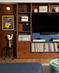Living room with a wooden shelving unit, TV, vinyl records, colorful chair, and decorative items.