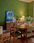 Dining area with a round wooden table, green chairs, a vase of flowers, and a green accent wall.