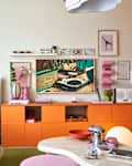 Colorful living room featuring an orange media console, a pink vase with flowers, and a retro record player artwork.