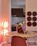 Modern dining area featuring a round table, pink chairs, decorative plates on the wall, and a cozy armchair.